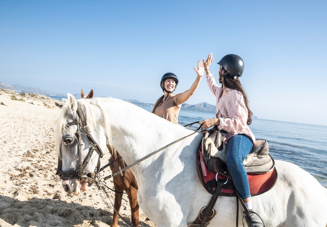 Freundinnen reiten an einem sonnigen Tag am Strand von Mallorca gemeinsam am Meer